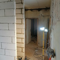 LENDOM Remonty-Wykończenia - Wnętrze w trakcie przebudowy, widoczne murowane ściany z betonu komórkowego, przygotowane do dalszych prac wykończeniowych, z widocznymi narzędziami i oświetleniem halogenowym.