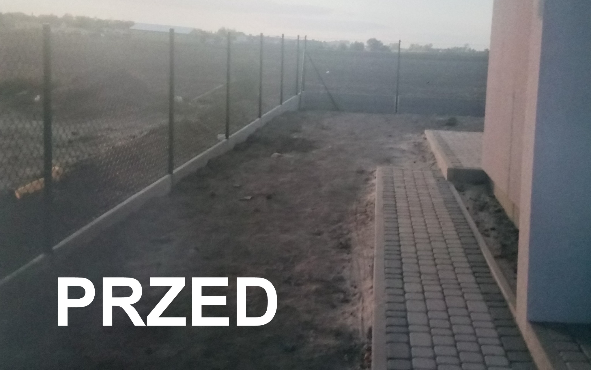 Teren przed domem z widocznym fragmentem ułożonej kostki brukowej przy ścianie budynku oraz siatką ogrodzeniową na betonowej podmurówce, ziemia do wyrównania.