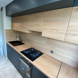 Happy Dreams - Nowoczesna kuchnia z drewnianymi frontami szafek i czarnymi elementami: zlew, bateria, płyta grzewcza i szafki. Jasna podłoga z marmurowym wzorem.