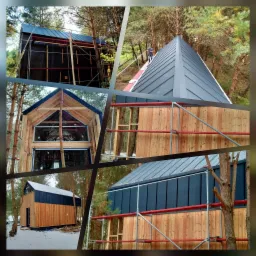 Montaż blachy na dachu nowoczesnego domu z drewnianą elewacją, widok z rusztowania na tle lasu, etap budowy.