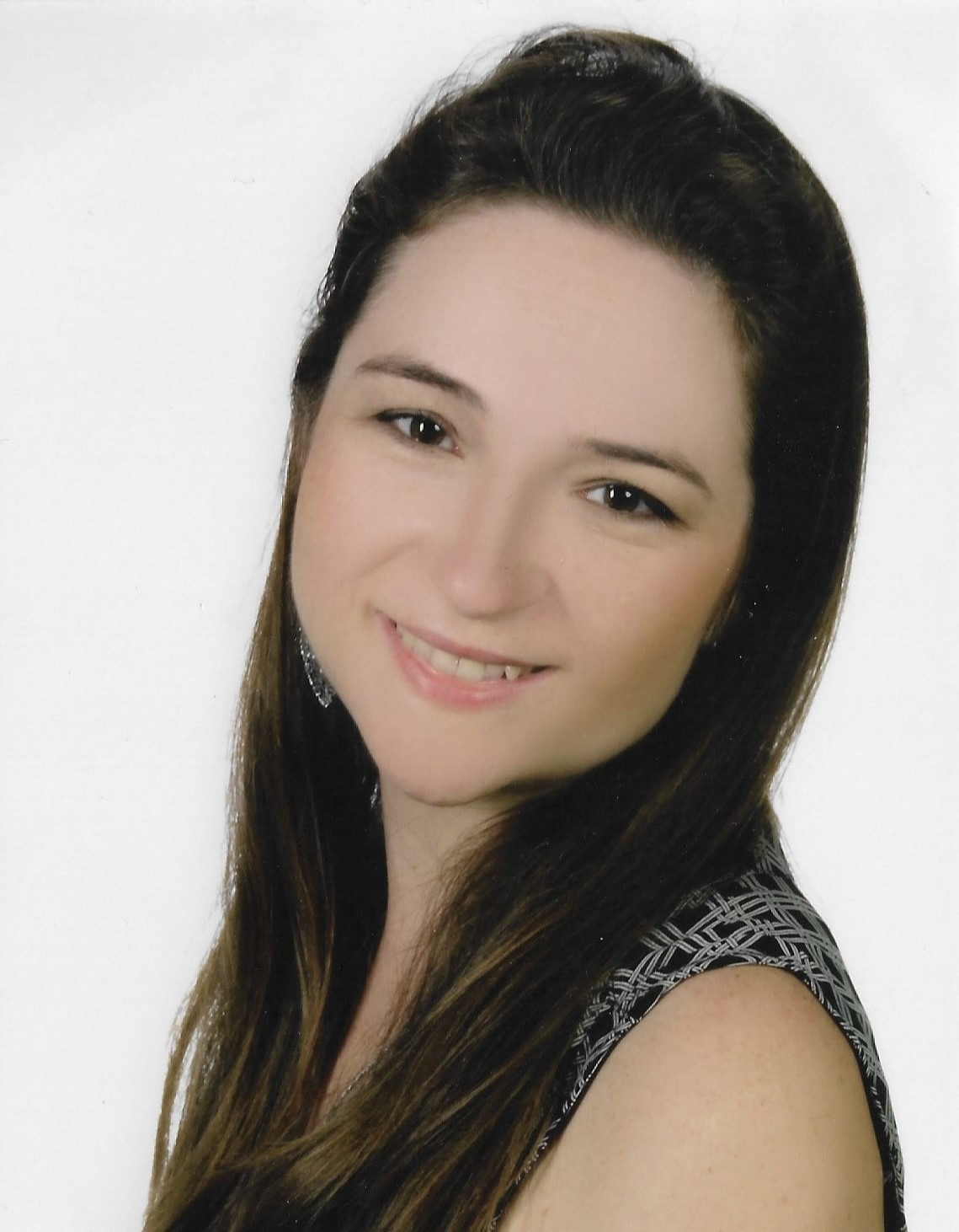 Portret uśmiechniętej kobiety z długimi brązowymi włosami, ubrana w bluzkę w geometryczny wzór, na białym tle.