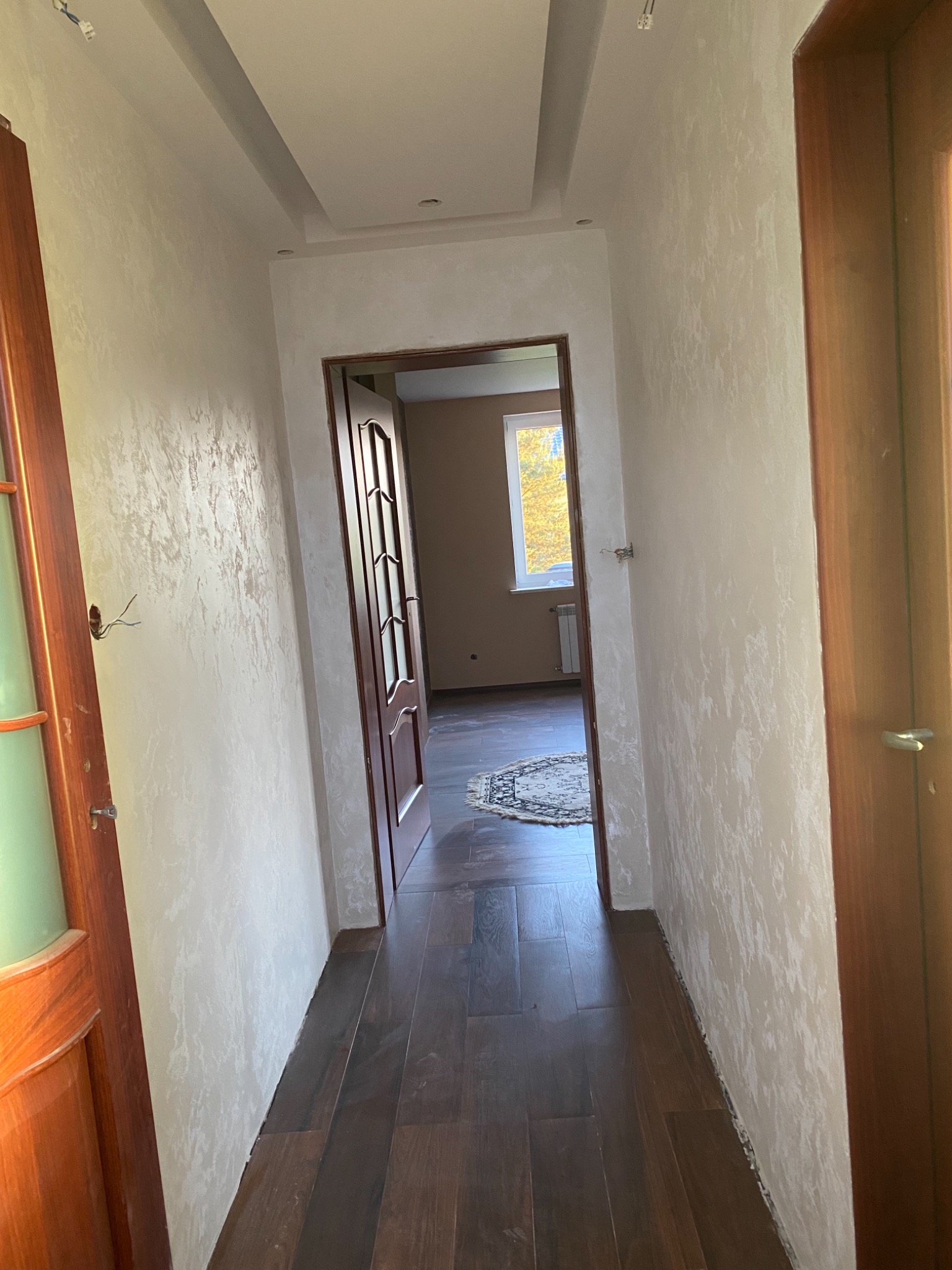 Korytarz po remoncie z dekoracyjnym tynkiem na ścianach, drewnianą podłogą i widokiem na pokój z dywanem i oknem.