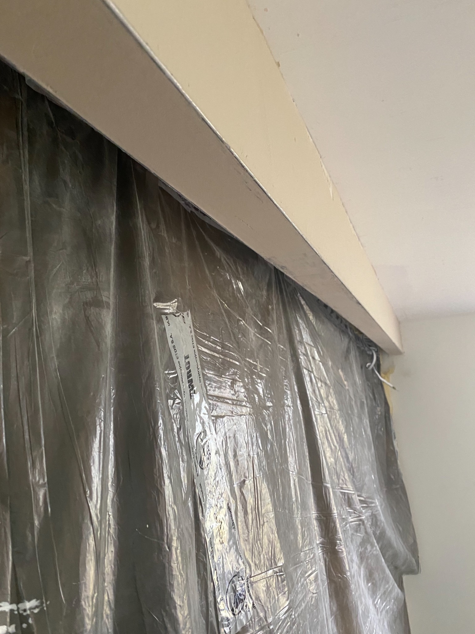 Przygotowanie do prac remontowych: ściana zabezpieczona folią malarską, widoczna listwa sufitowa i fragment sufitu.