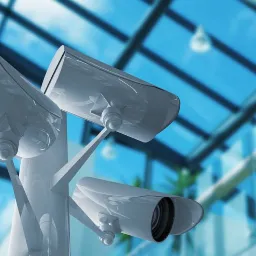 Trzy białe kamery CCTV zamontowane wewnątrz nowoczesnego biurowca z przeszklonym dachem i balkonem, skierowane w różnych kierunkach.