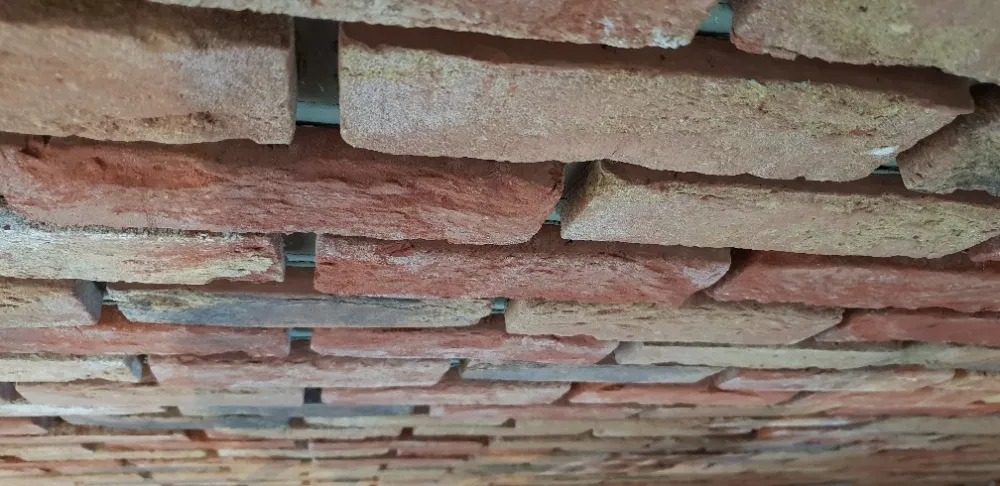 Wykończona ściana z dekoracyjnej cegły w odcieniach czerwieni i beżu, z wyraźnie widoczną fakturą i fugami. Ujęcie z dołu.