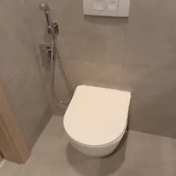 Wisząca toaleta z bidetką i podtynkowym spłukiwaniem w łazience wykończonej szarymi płytkami.