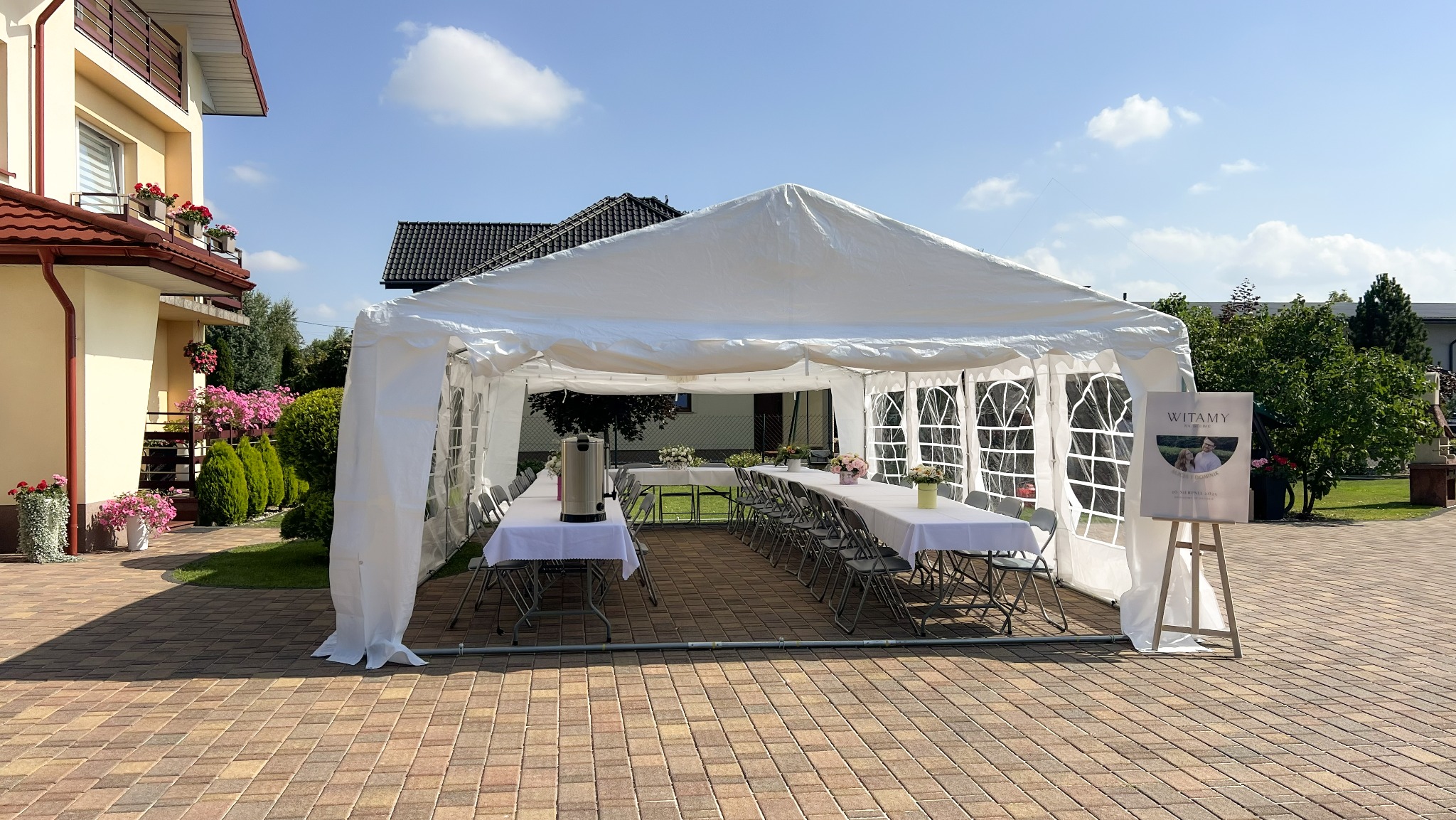 Biały namiot imprezowy 5x8 m z wyposażeniem: stoły z obrusami, krzesła, oświetlenie i dekoracje, ustawiony na zewnątrz, gotowy na przyjęcie.