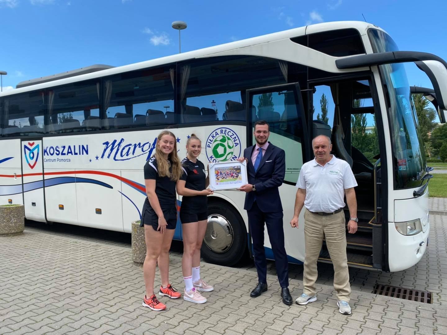 Wręczenie wyróżnienia przez przedstawicieli firmy transportowej Młynom Stoisław Koszalin na tle autokaru z logo drużyny piłki ręcznej.
