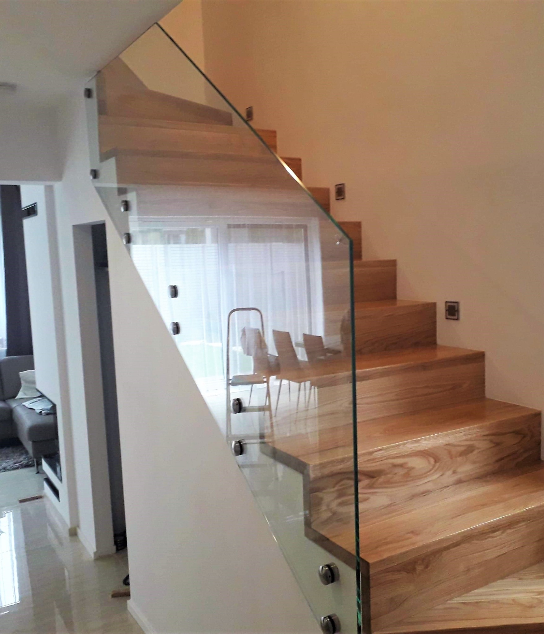 Nowoczesne drewniane schody z balustradą ze szkła hartowanego, mocowaną na metalowych uchwytach punktowych, widok z dołu.