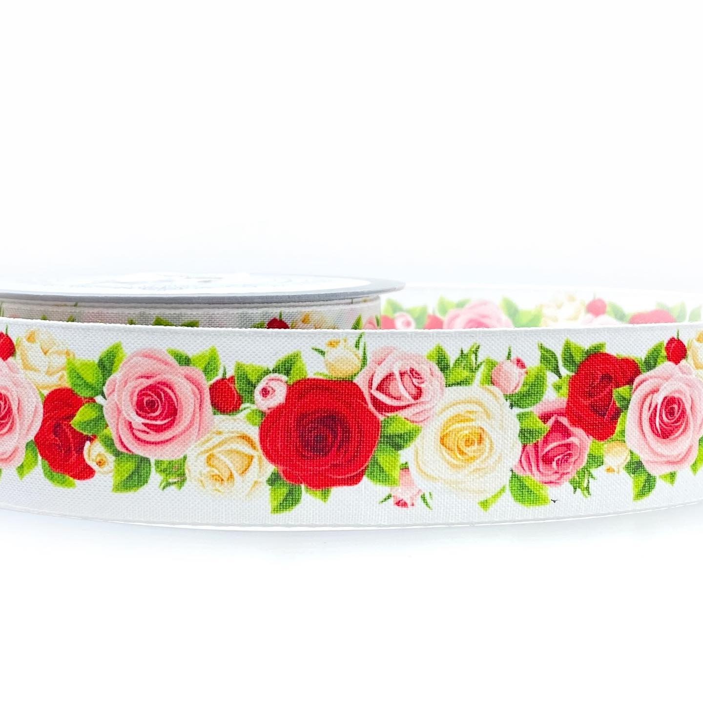 Rolka białej wstążki z nadrukiem róż w odcieniach czerwieni, różu i bieli, bliski kadr, widoczna faktura tkaniny.