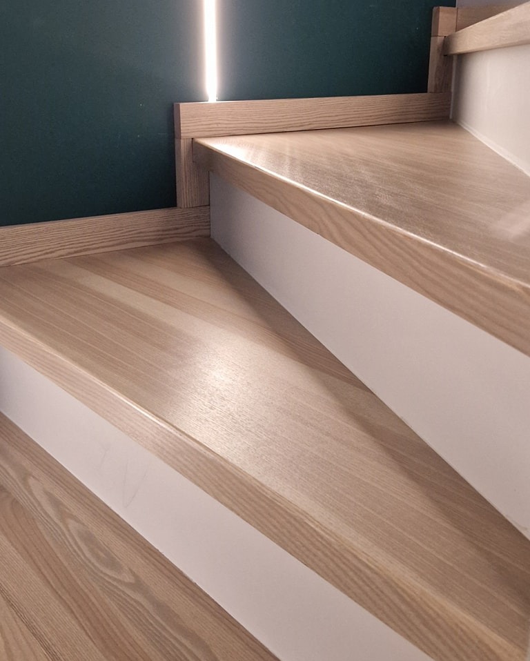 Detal drewnianych schodów z białymi podstopnicami i oświetleniem LED w tle, widok z góry.