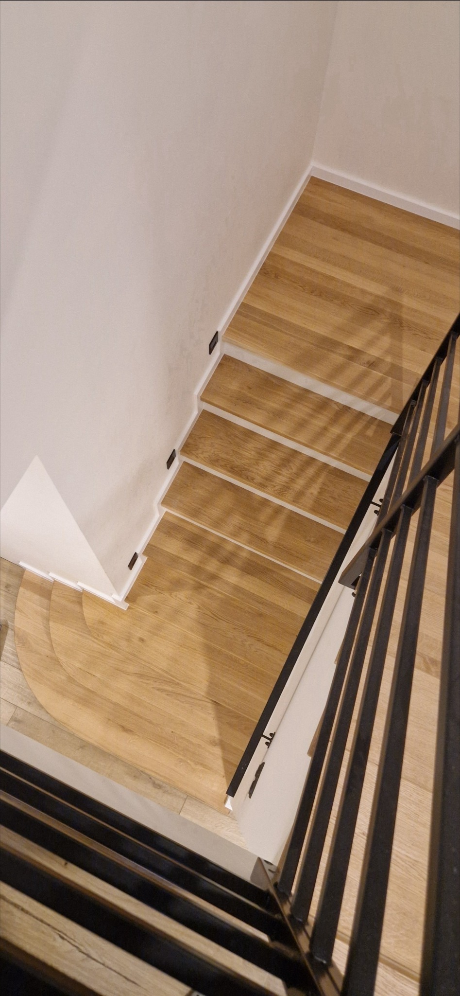 Drewniane schody z podświetleniem stopni i metalową balustradą, widok z góry.