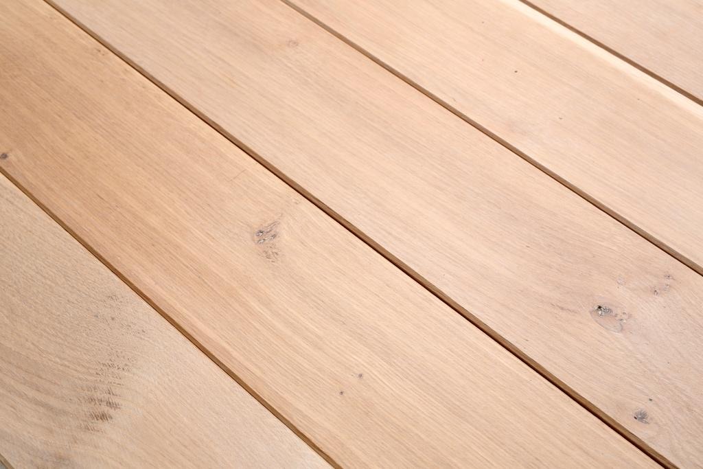 Jasne, drewniane deski podłogowe ułożone równolegle, z widocznymi naturalnymi sękami i delikatnym usłojeniem.