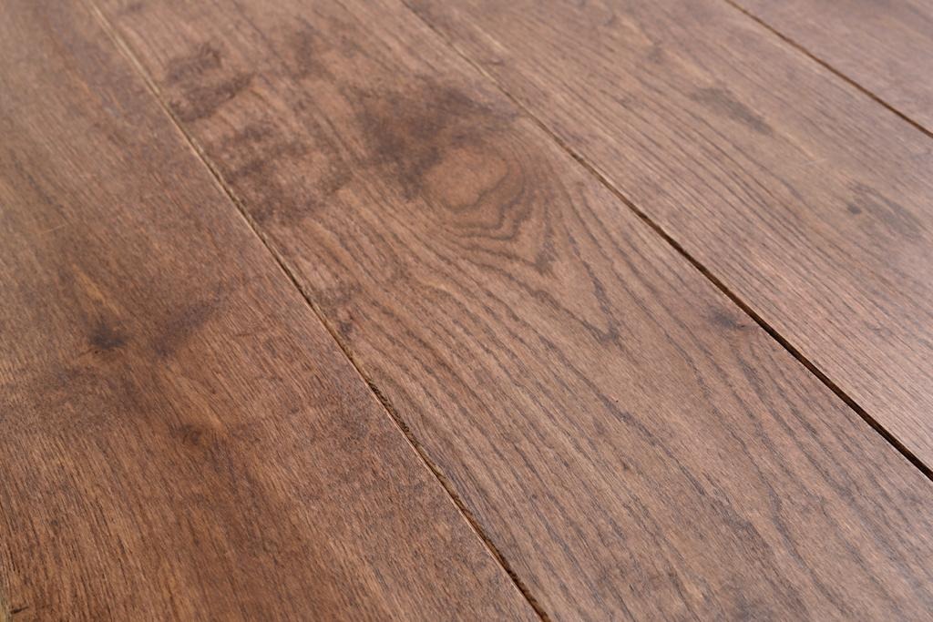 Ujęcie z bliska ciemnobrązowej, lakierowanej podłogi z wyraźnym usłojeniem drewna i widocznymi szczelinami między deskami.