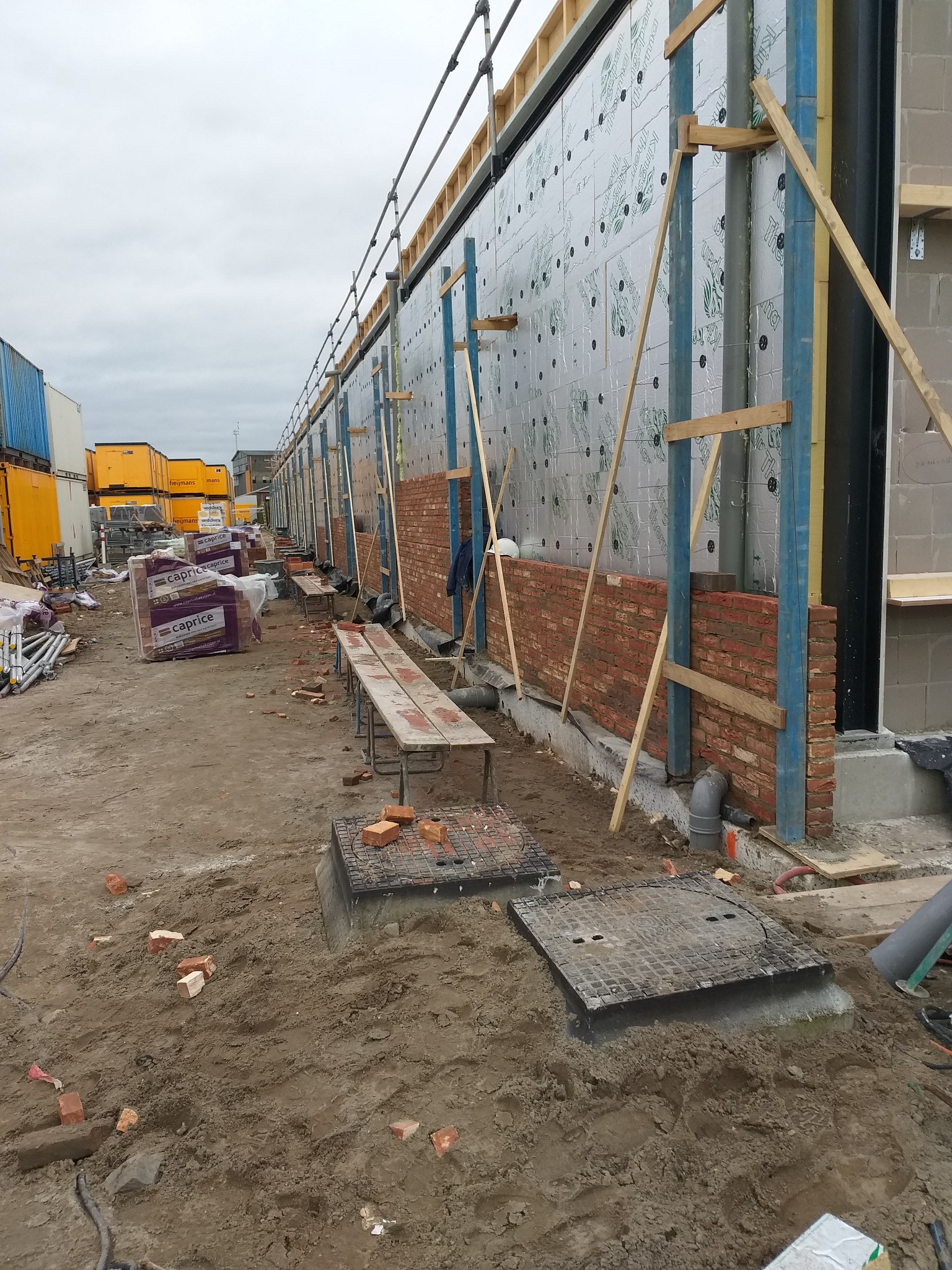 Wznoszenie muru z czerwonej cegły na placu budowy, widoczne rusztowania, izolacja termiczna i materiały budowlane