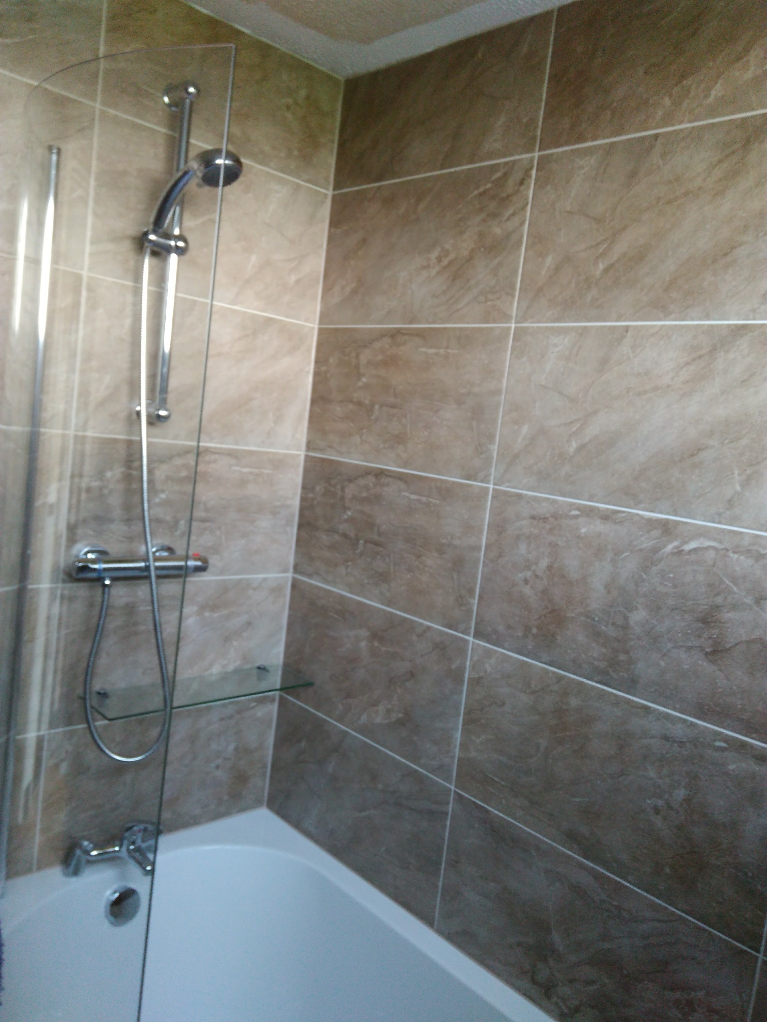 Wykończona łazienka z beżowymi płytkami imitującymi marmur, szklanym parawanem nawannowym i chromowaną armaturą.