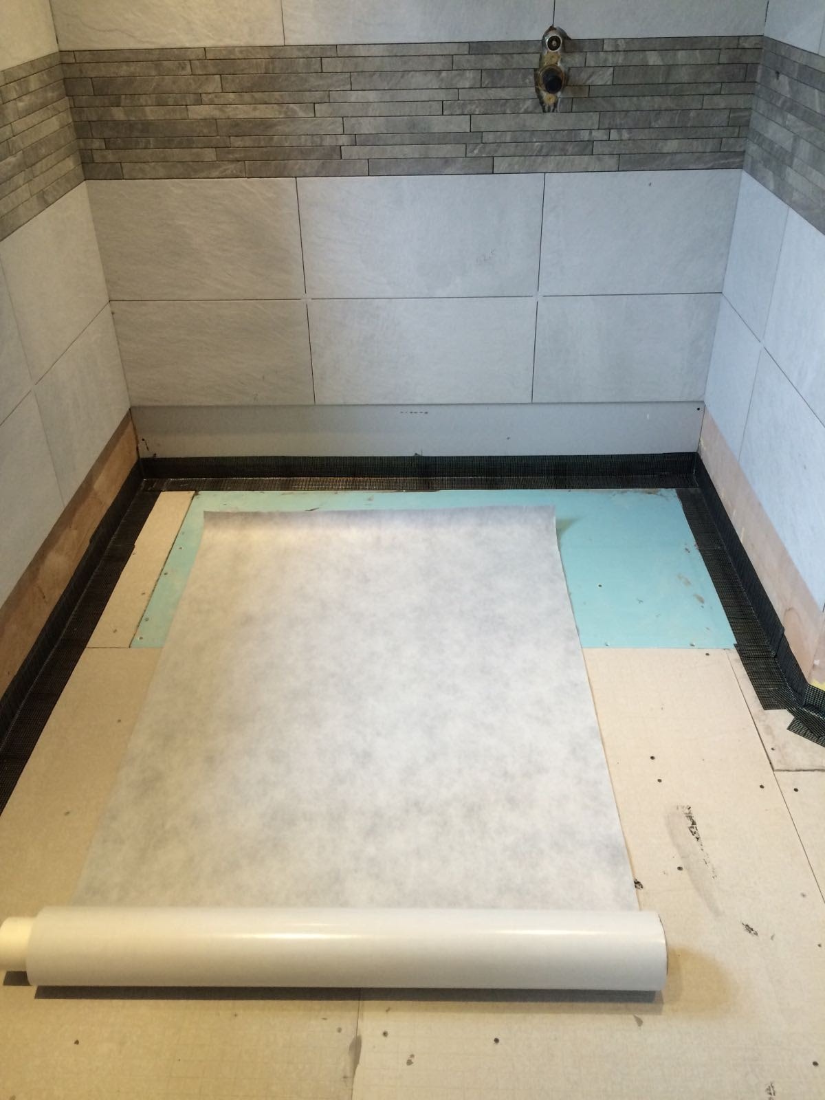 Przygotowanie podłoża w łazience: rozłożona membrana hydroizolacyjna na podłodze, widoczne płytki na ścianach i siatka uszczelniająca przy krawędziach, rura wystająca ze ściany.