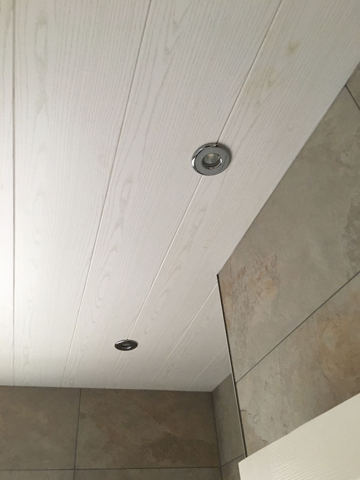 Drewnopodobny panel sufitowy z dwoma chromowanymi halogenami, w tle ściana wyłożona płytkami imitującymi kamień.