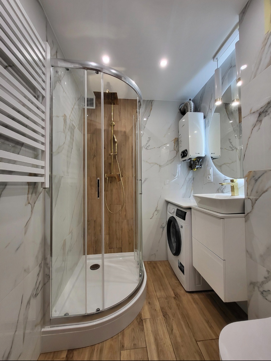 Nowoczesna łazienka z kabiną prysznicową, marmurowymi płytkami i drewnianą ścianą prysznica. Umywalka z szafką, pralka i piec gazowy w aranżacji.