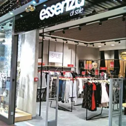 Wejście do butiku odzieżowego Essenza di Stile z ekspozycją ubrań i dekoracyjnymi złotymi kulami wiszącymi z sufitu, widoczny plakat z napisem SALE.