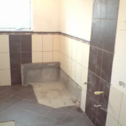 Łazienka w trakcie remontu w Kielcach: częściowo ułożona ciemna glazura podłogowa w romby, białe i ciemne płytki ścienne układane pionowo, widoczne niedokończone prace przy wnęce.