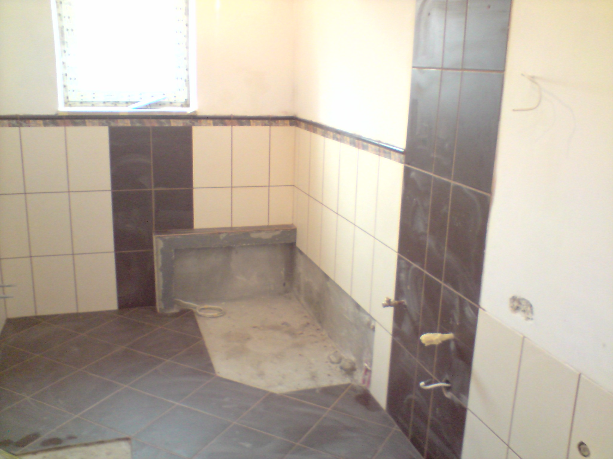 Łazienka w trakcie remontu w Kielcach: częściowo ułożona ciemna glazura podłogowa w romby, białe i ciemne płytki ścienne układane pionowo, widoczne niedokończone prace przy wnęce.