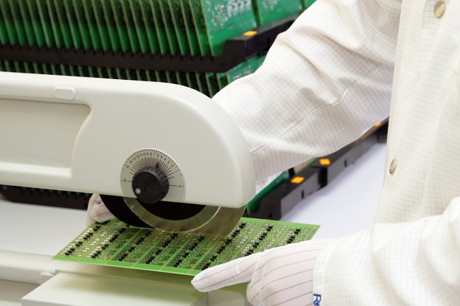 Operator w rękawicach i fartuchu laboratoryjnym oddziela płytkę drukowaną za pomocą białego, precyzyjnego separatora z regulacją kąta.