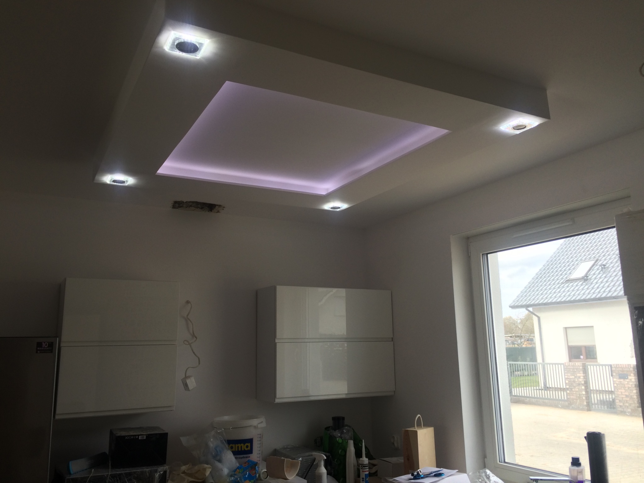 Podwieszany sufit z oświetleniem LED w kształcie kwadratu, cztery punktowe lampy, białe szafki kuchenne w tle, widok z dołu.