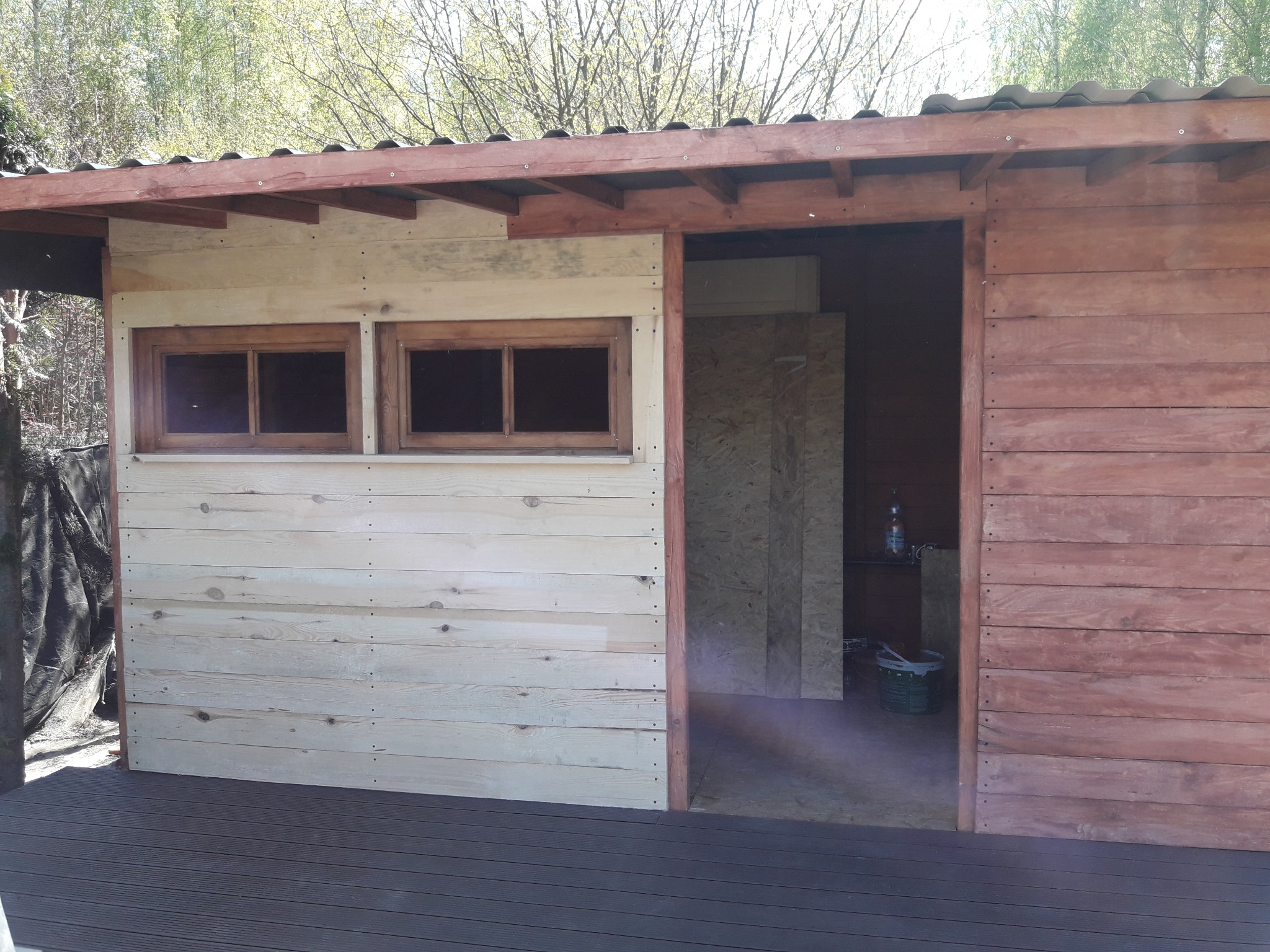 Budowa drewnianej konstrukcji z widocznymi dwoma oknami i częściowo pomalowaną elewacją na zewnątrz, widoczny fragment tarasu i elementy wyposażenia wewnątrz.