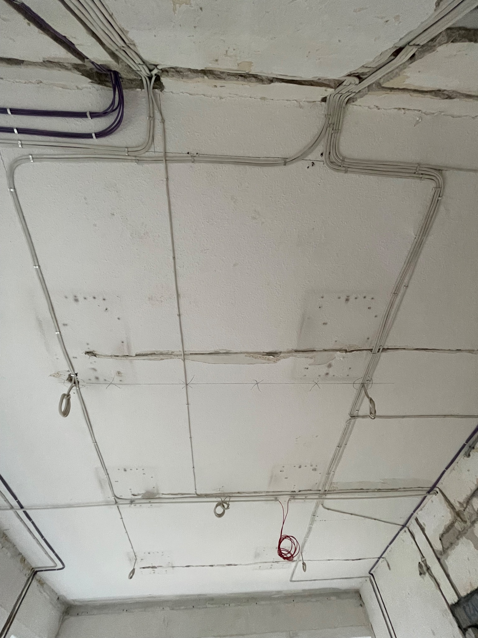 Układanie przewodów elektrycznych w peszlach na suficie w surowym stanie, widoczne kable fioletowe i szare oraz uchwyty mocujące.
