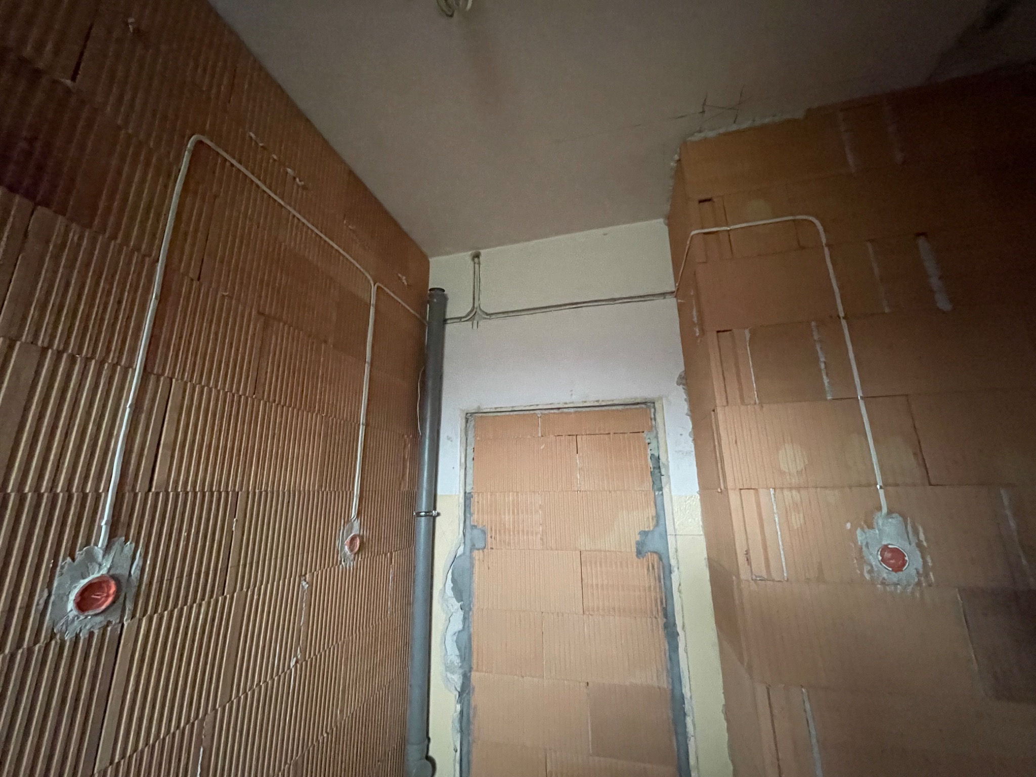 Wnętrze w trakcie remontu: instalacja elektryczna w peszlach prowadzona po ścianach z pustaków ceramicznych, widoczne puszki instalacyjne z czerwonymi zaślepkami.