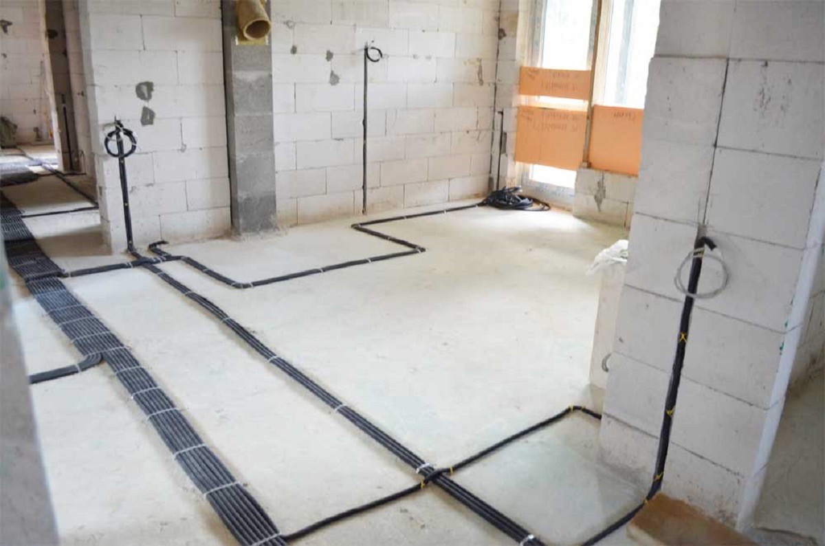 Wnętrze w stanie surowym z widoczną instalacją elektryczną: kable prowadzone po podłodze i ścianach z betonu komórkowego, część kabli ułożona w wiązki.