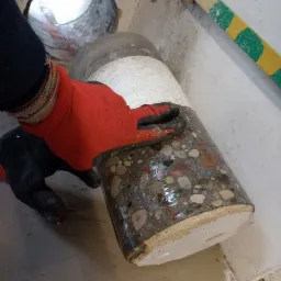 Rdzeń wywiercony w betonie, trzymany w rękawicy roboczej, widoczny otwór w ścianie i przewód z oznaczeniami.