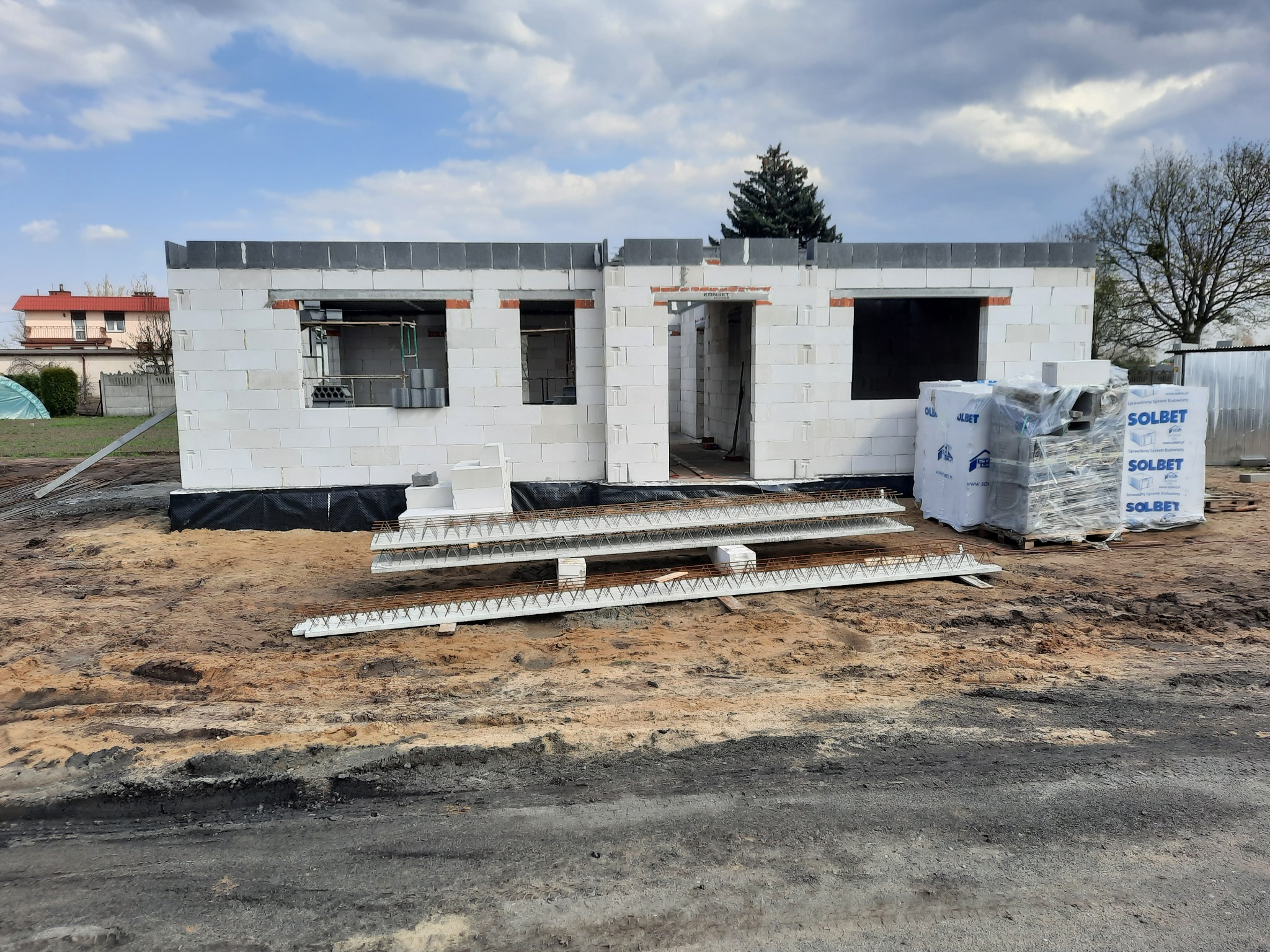 Wznoszenie ścian budynku z betonu komórkowego Solbet, widoczne nadproża i zbrojenia, teren budowy w trakcie prac.