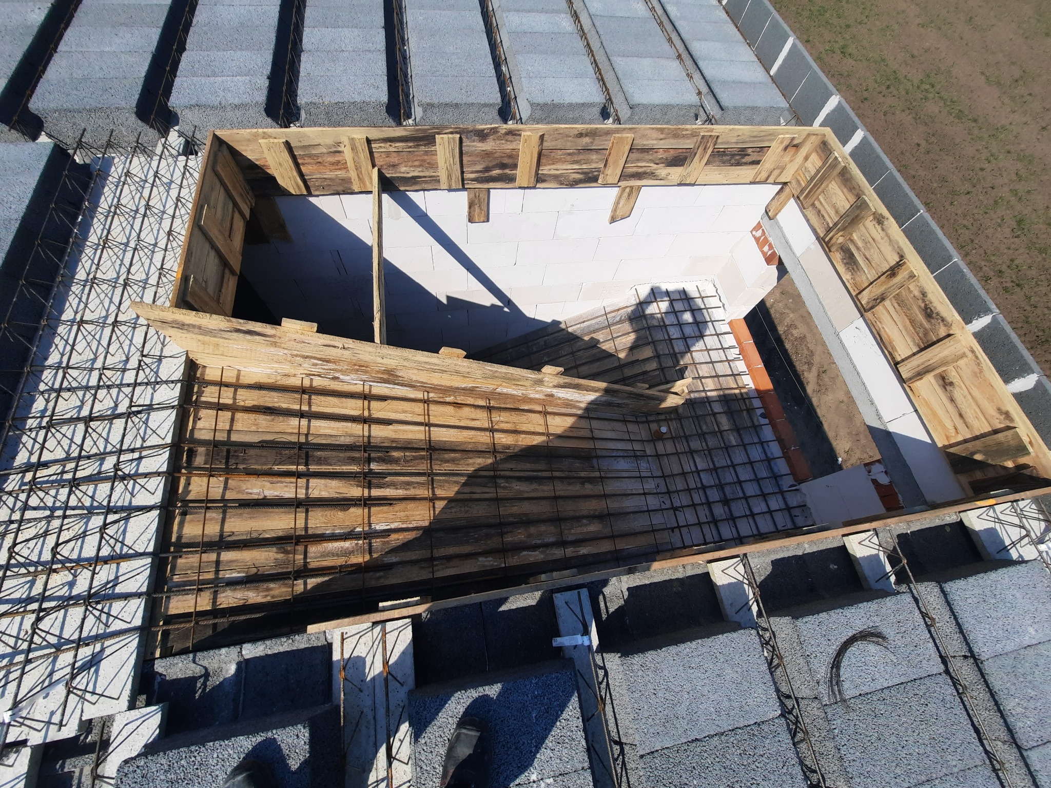 Widok z góry na wieniec stropowy w trakcie budowy, z drewnianym szalunkiem i zbrojeniem, otoczony bloczkami betonowymi.