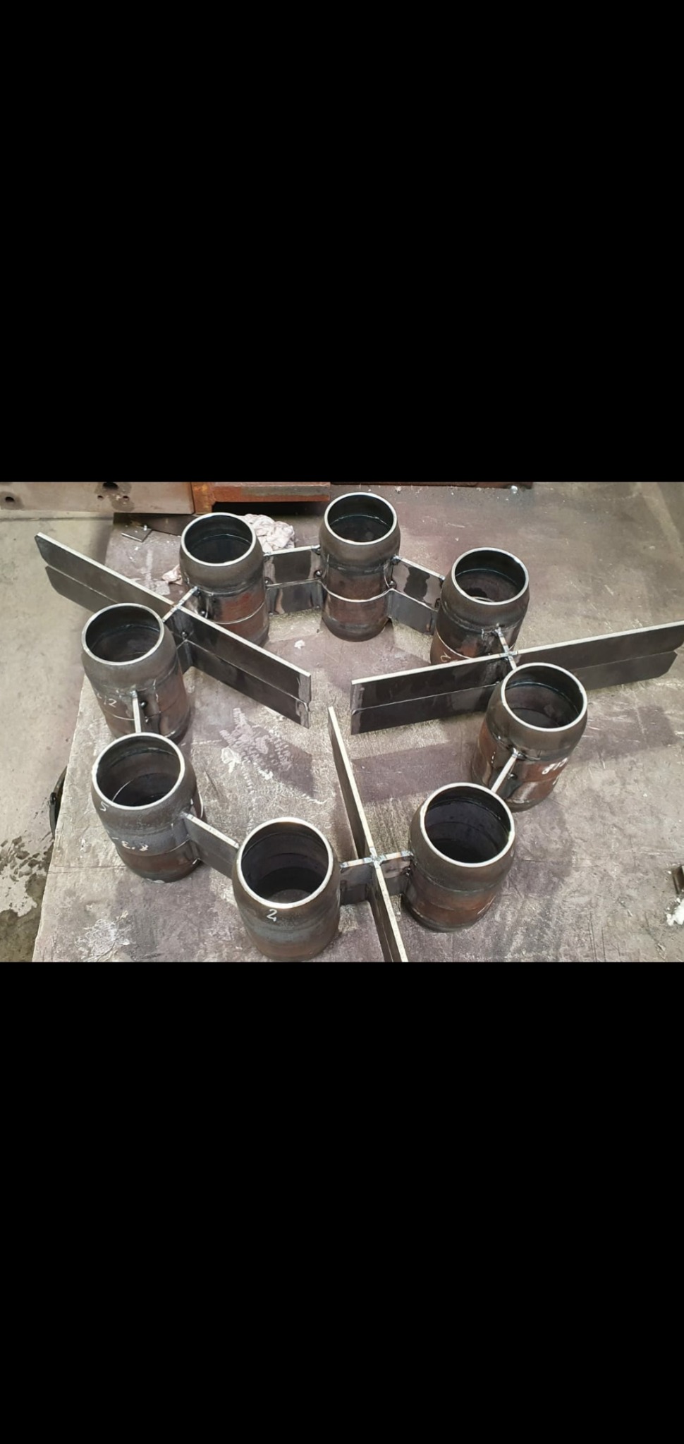 Metalowe elementy konstrukcyjne, cylindryczne i płaskie, połączone spawami, leżące na metalowym stole warsztatowym w hali produkcyjnej.