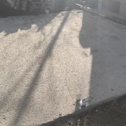 Wylany betonowy fundament z metalowymi uchwytami mocującymi, widoczne deski szalunkowe i cień padający na powierzchnię.