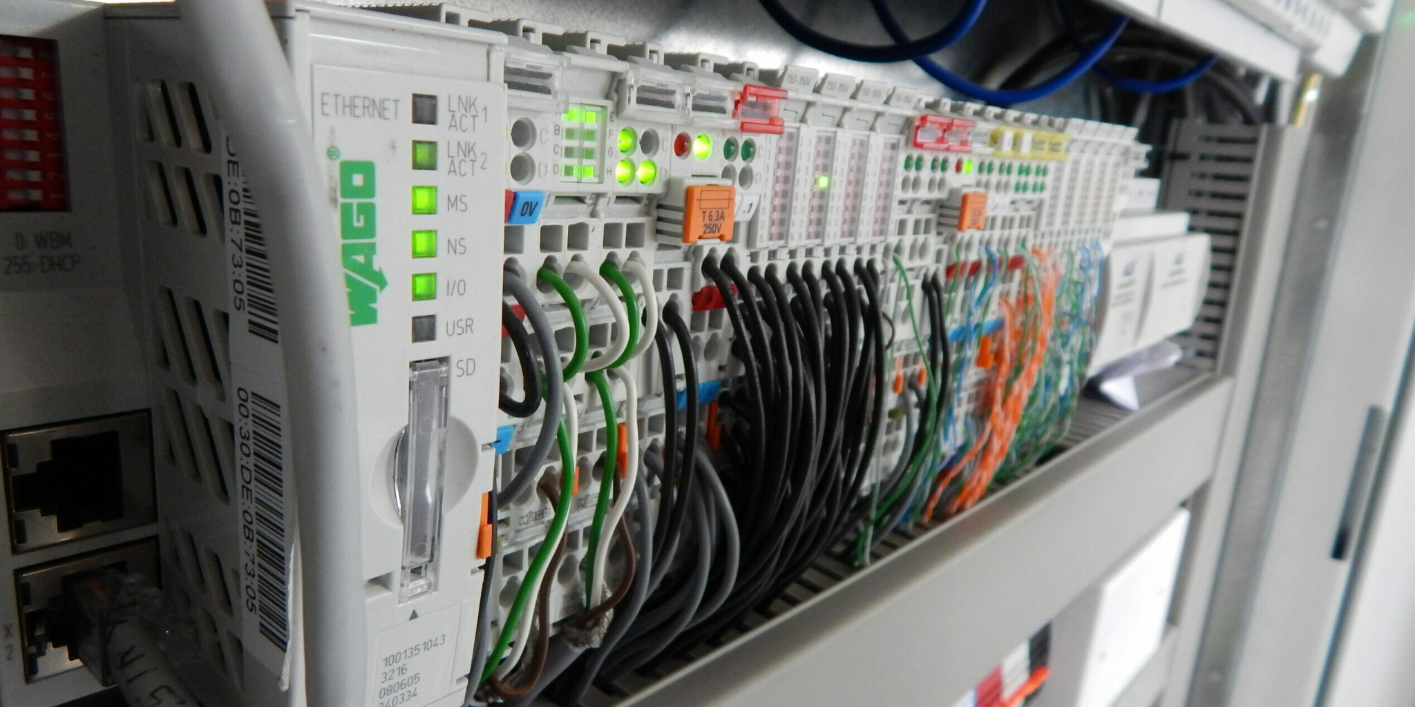 Szczegółowe ujęcie panelu sterowania WAGO z podłączonymi przewodami o różnych kolorach, widoczne diody LED wskazujące status połączeń, umieszczonego w szafie sterowniczej.
