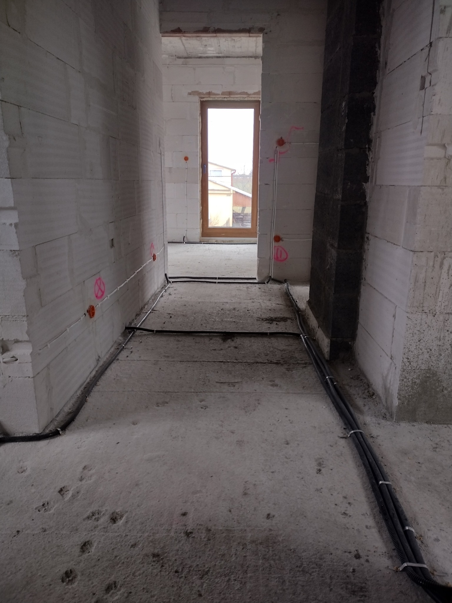 Wnętrze surowego budynku w trakcie prac, widoczne kable elektryczne prowadzone wzdłuż ściany i podłogi, pomarańczowe puszki instalacyjne z oznaczeniami na ścianach z betonu komórkowego, widok...