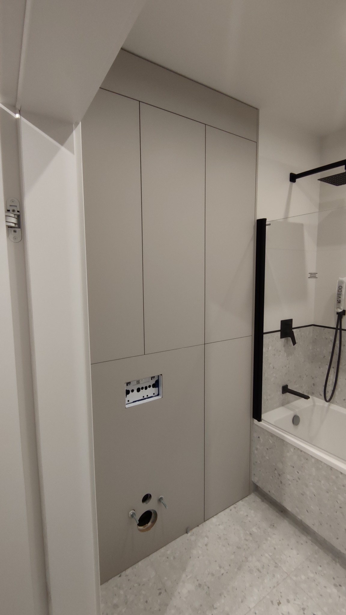 Szara zabudowa meblowa w łazience w trakcie montażu, widoczne otwory na instalacje i brakującą armaturę, minimalistyczny design.