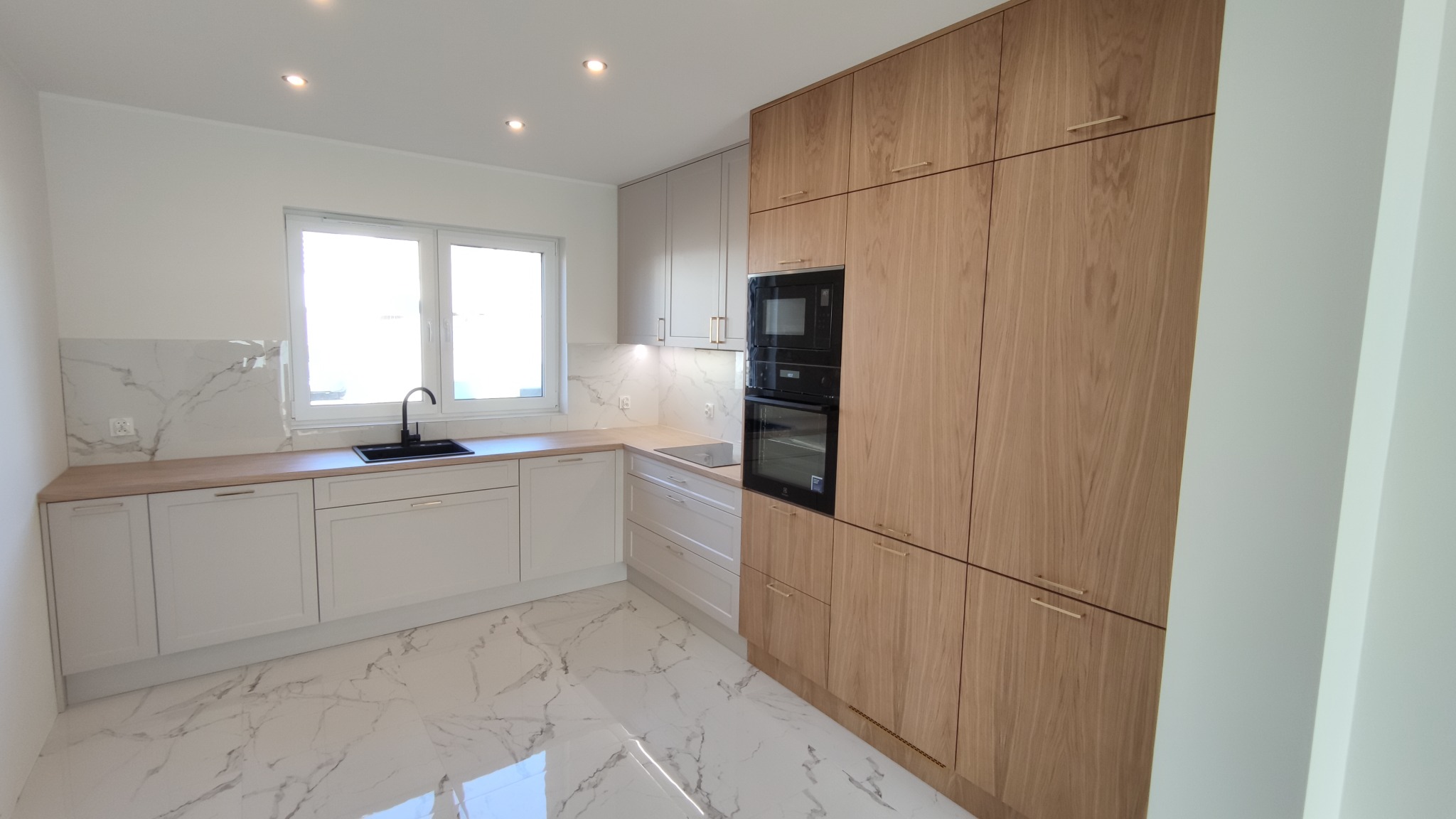 Nowoczesna kuchnia z białymi i drewnianymi frontami, marmurową podłogą i backsplashiem, czarną armaturą i wbudowanym piekarnikiem.