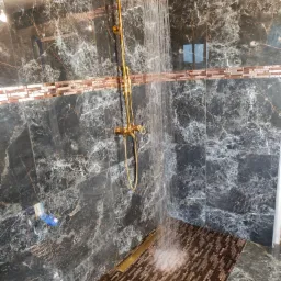 Luksusowy prysznic z deszczownicą w odcieniach złota i czarnego marmuru, z mozaiką w kolorze miedzi na podłodze i dekoracyjnym pasem na ścianie.