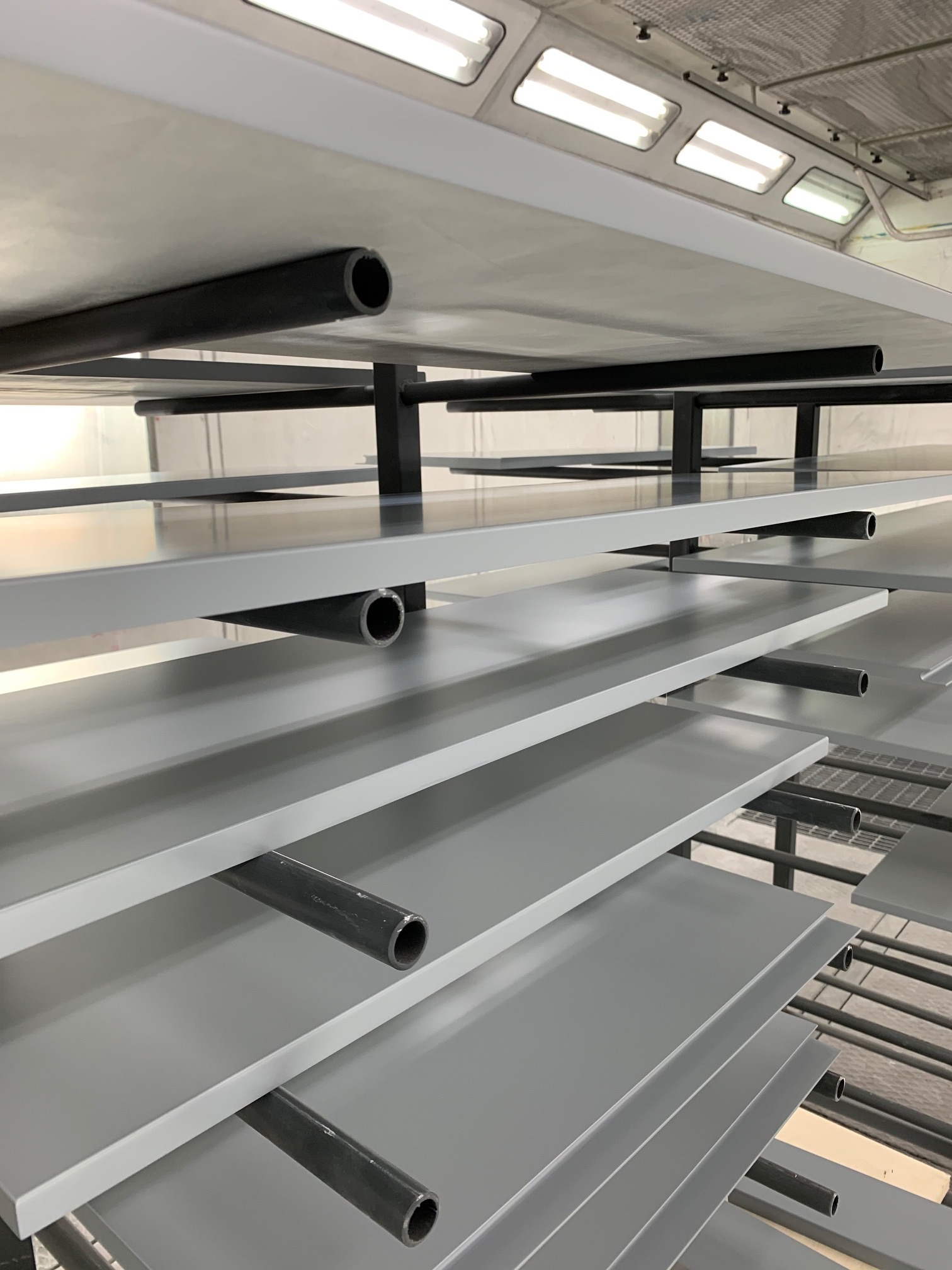 Półki z pomalowanymi na szaro elementami meblowymi, suszone w specjalnej suszarni z oświetleniem przemysłowym.
