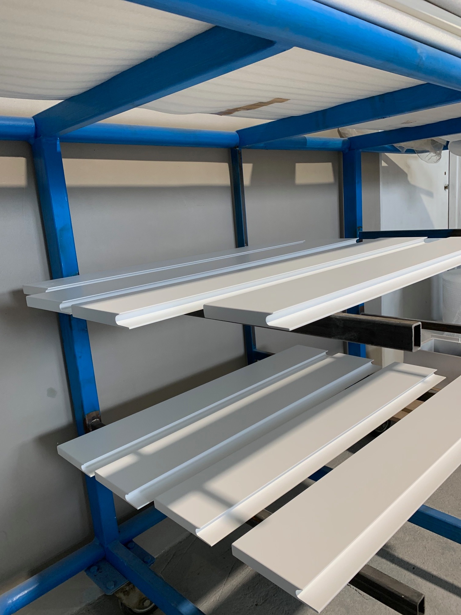 Białe, pomalowane listwy przypodłogowe na niebieskim regale w warsztacie, gotowe do wyschnięcia.