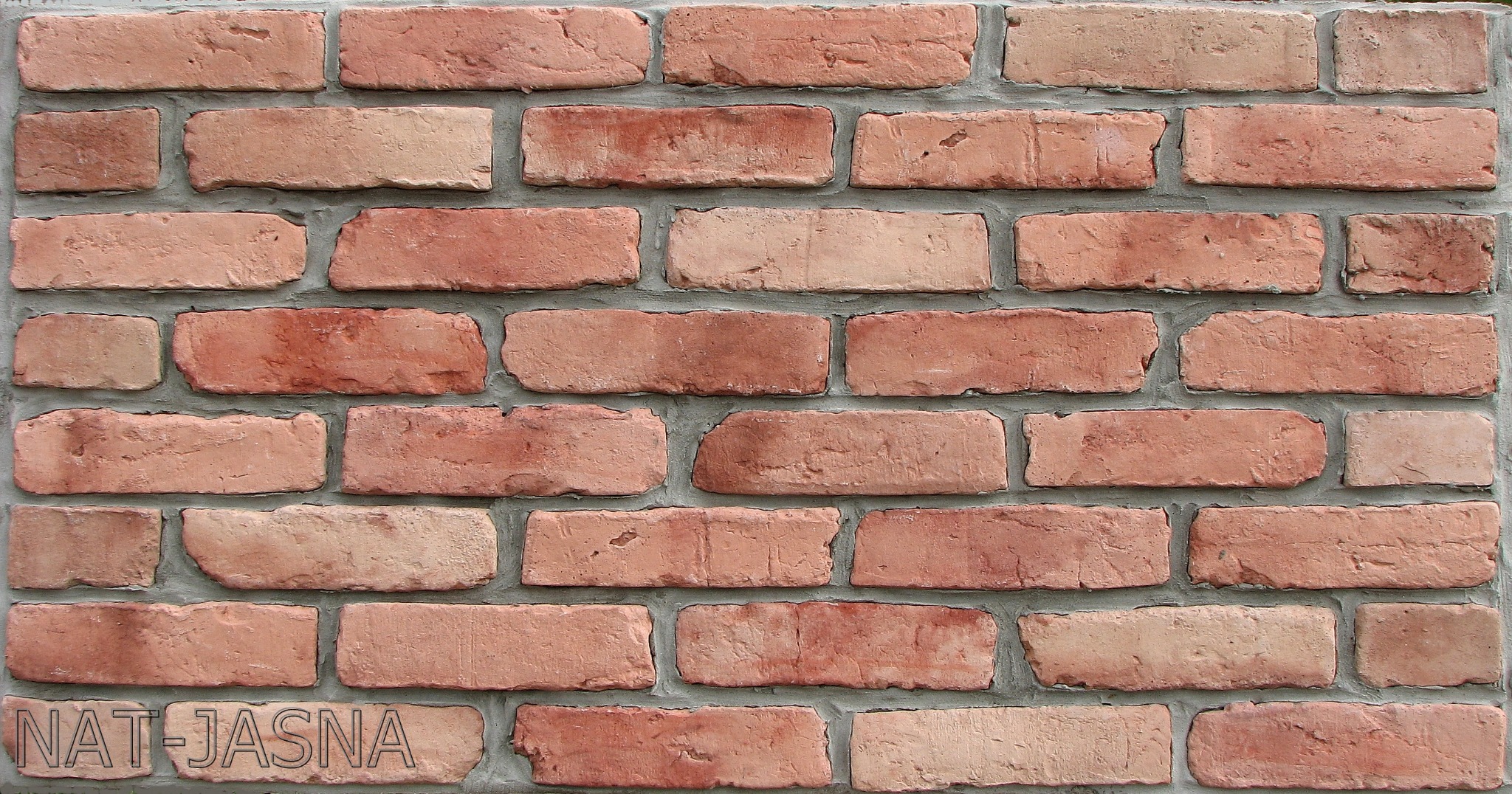 Mur z cegieł klinkierowych w odcieniach czerwieni i różu, spoiny wypełnione szarą zaprawą. Widoczne delikatne nierówności powierzchni cegieł.
