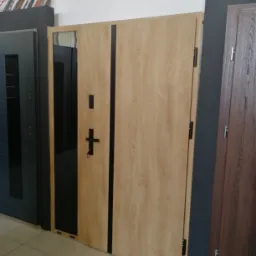Wystawa trzech modeli drzwi wewnętrznych: jasne drewno z czarnym pionowym pasem, ciemny grafit z przeszkleniem i ciemne drewno. Prezentacja w salonie sprzedaży.