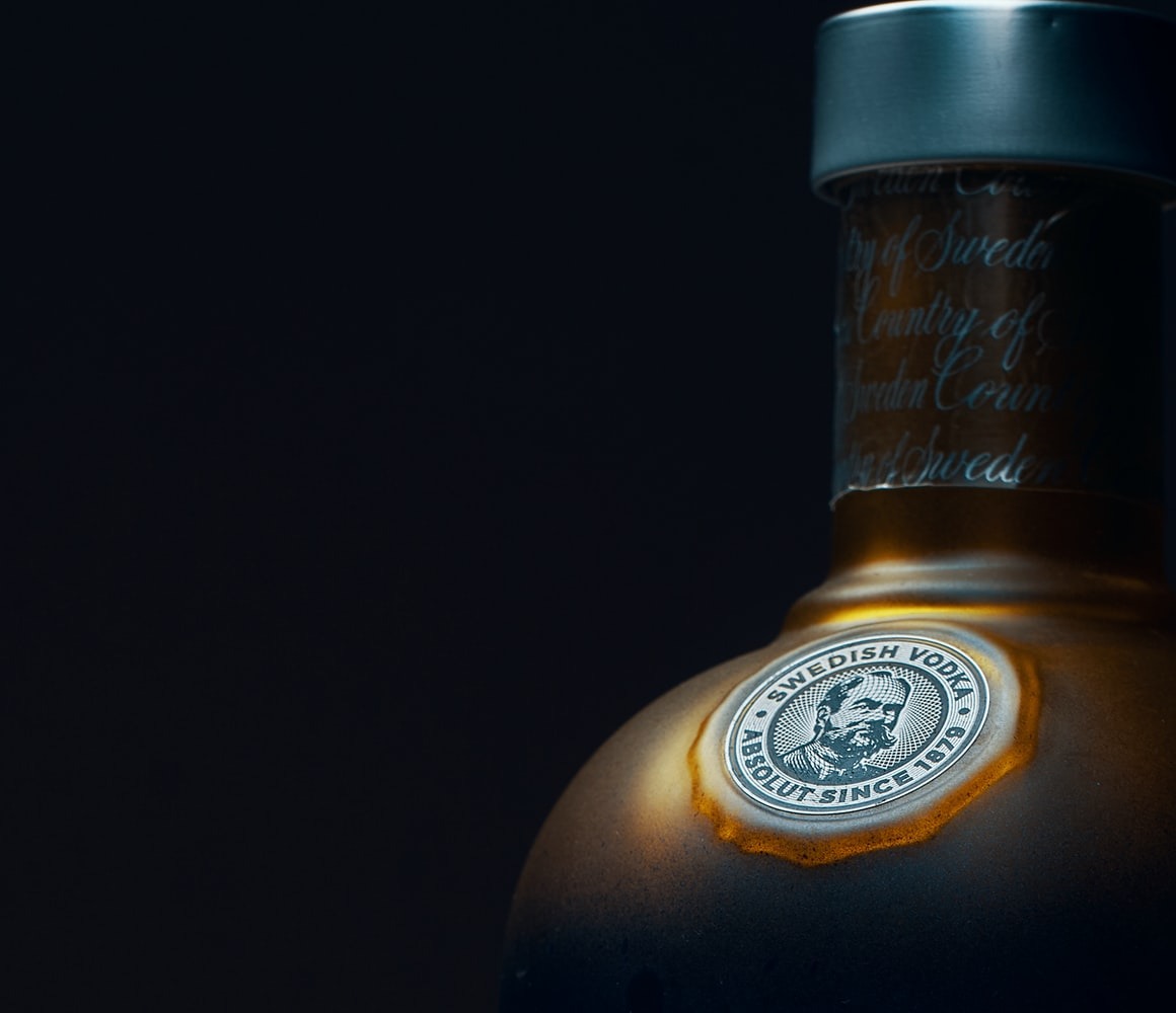 Butelka wódki Absolut z bliska, etykieta z portretem założyciela i napisem 'Swedish Vodka Since 1879' w świetle punktowym na ciemnym tle.