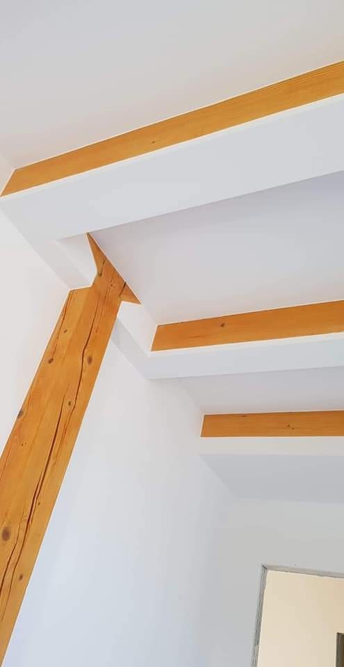 Biały sufit z drewnianymi belkami i skośną podporą, widoczne połączenie belek ze ścianą i sufitem, minimalistyczny design.