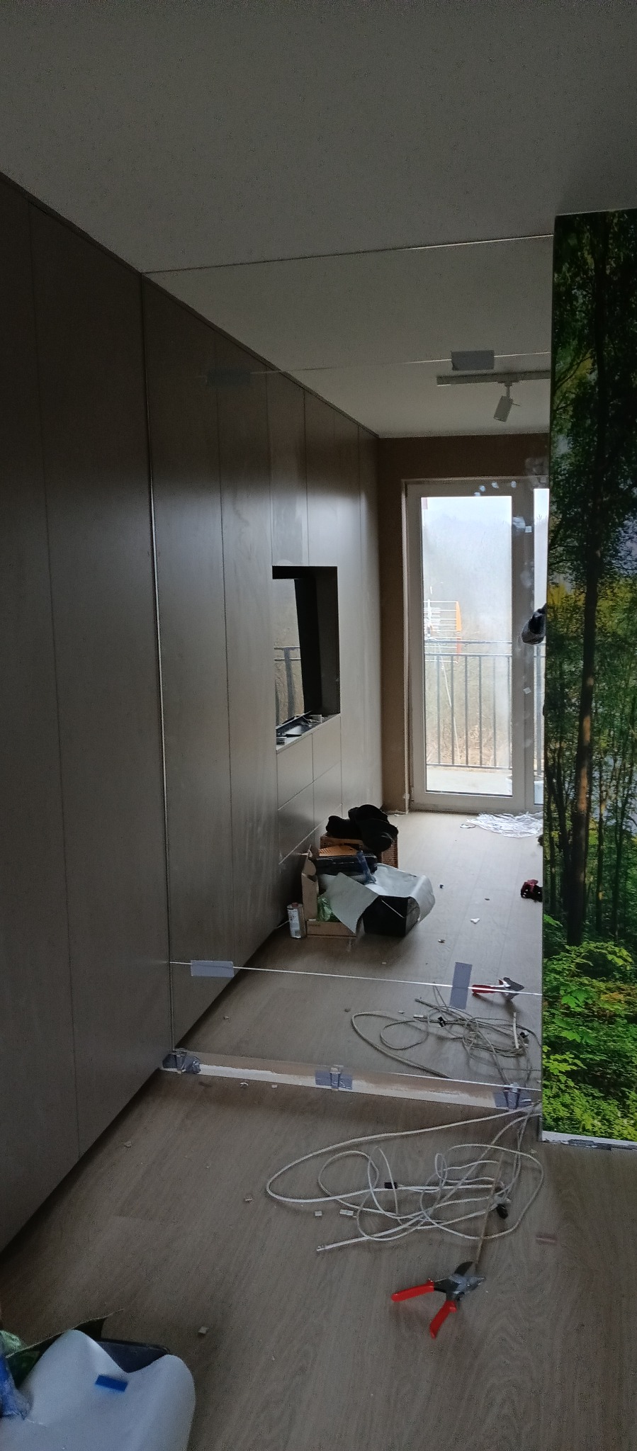 Montaż lustra na ścianie w pokoju, widoczne kable, narzędzia i mocowania.