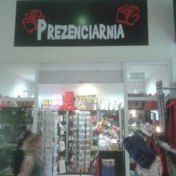 Studio Reklamy RED DOG - Wnętrze sklepu z prezentami 'Prezenciarnia', widoczny asortyment na półkach i regałach, nad wejściem szyld z nazwą i grafiką prezentów.